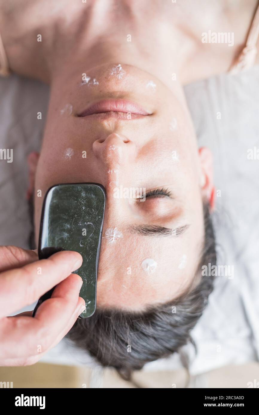 Young Caucasian woman getting facial treatment. Therapist doing skin scrape technique. Chinese