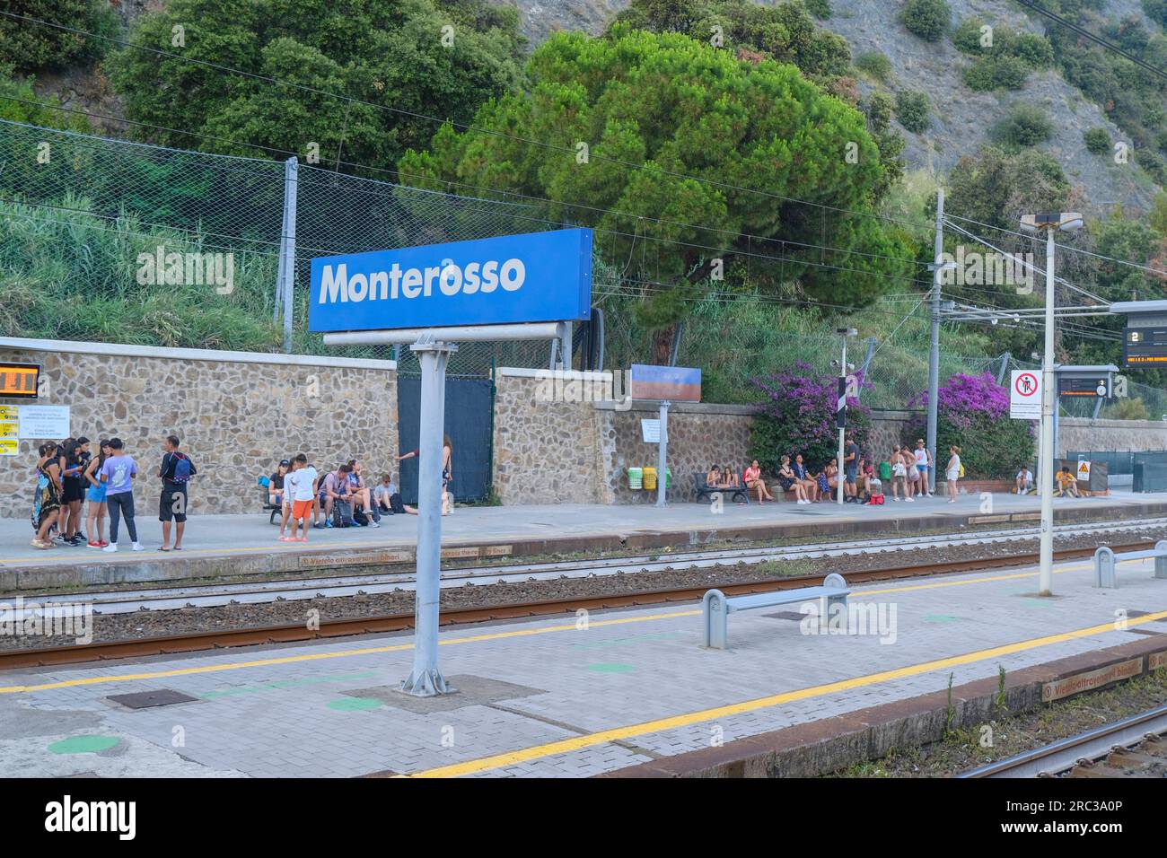 June 2023 Monterosso, Italy: Monterosso sign on the railway platform across the trains, station infrastructure, and passengers with suitcases Stock Photo