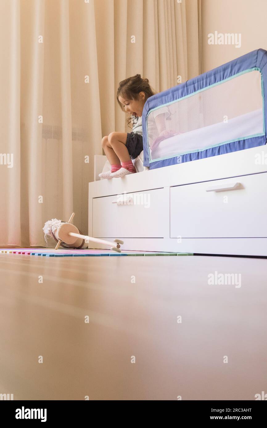 Small Caucasian girl playing in her bedroom, developing fine motor skills by getting on and off the bed. Copy space Stock Photo