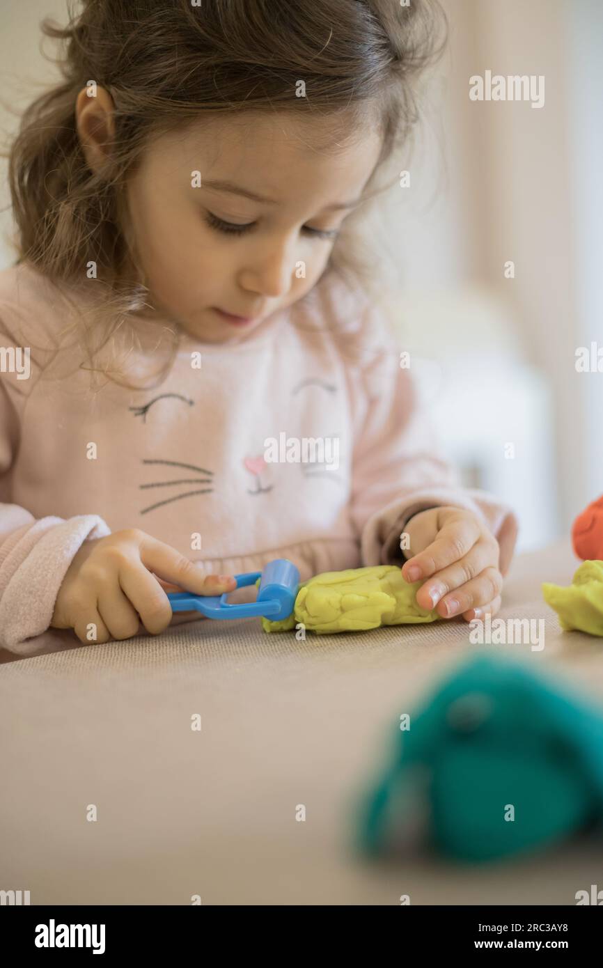 Caucasian child, two or three years old, playing and exercising fine motor skills with her hands, with clay and colored plasticine. Stock Photo