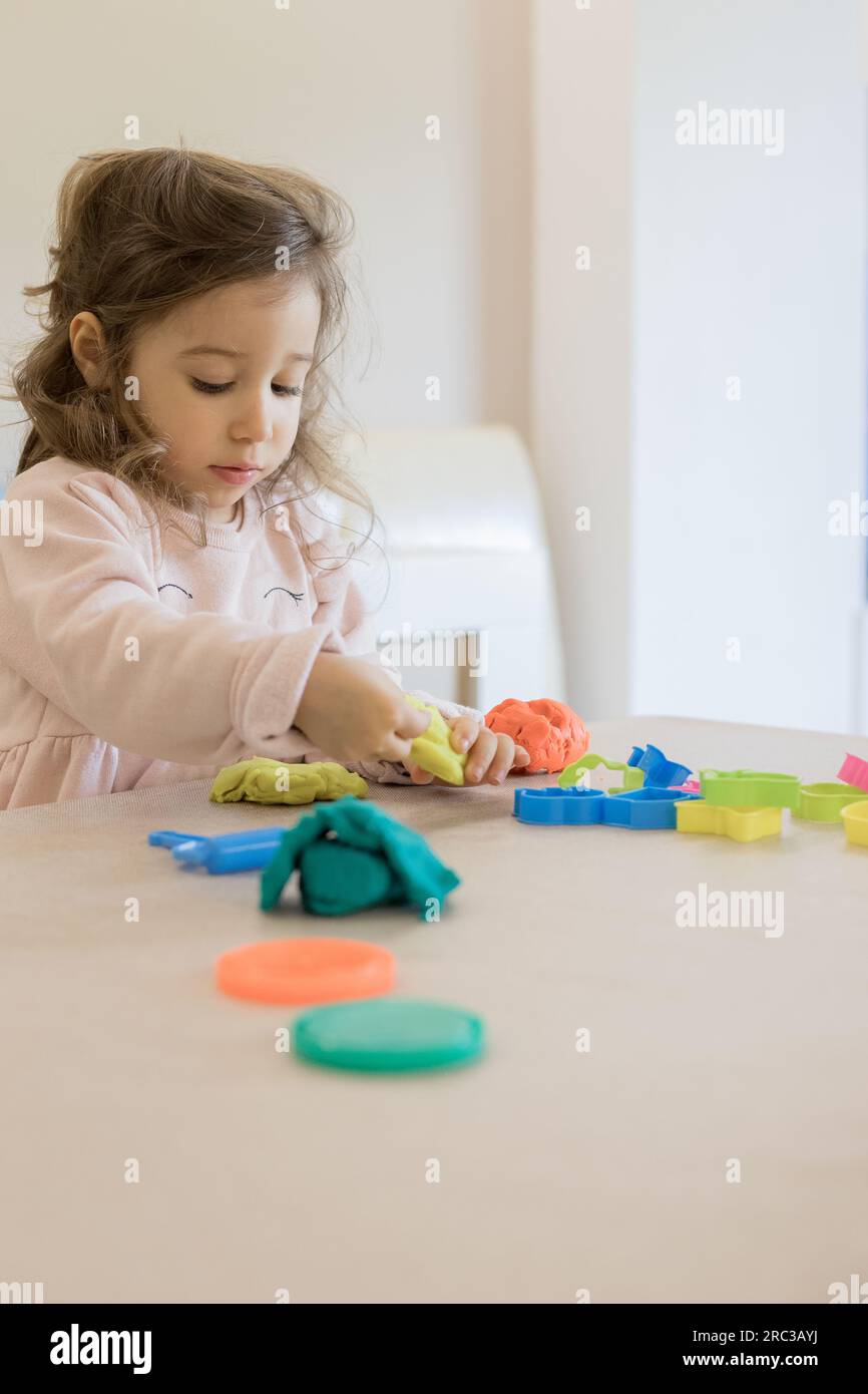Caucasian child, two or three years old, playing and exercising fine motor skills with her hands, with clay and colored plasticine. Stock Photo