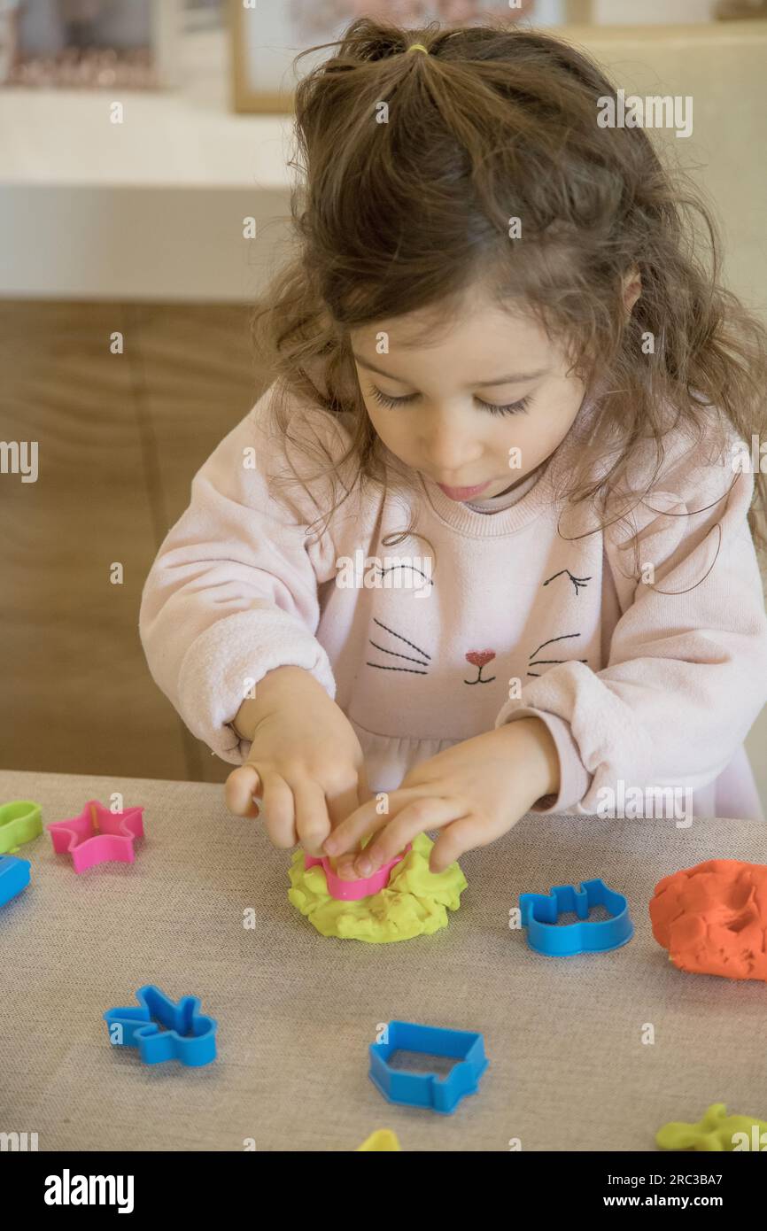 Caucasian child, two or three years old, playing and exercising fine motor skills with her hands, with clay and colored plasticine. Stock Photo