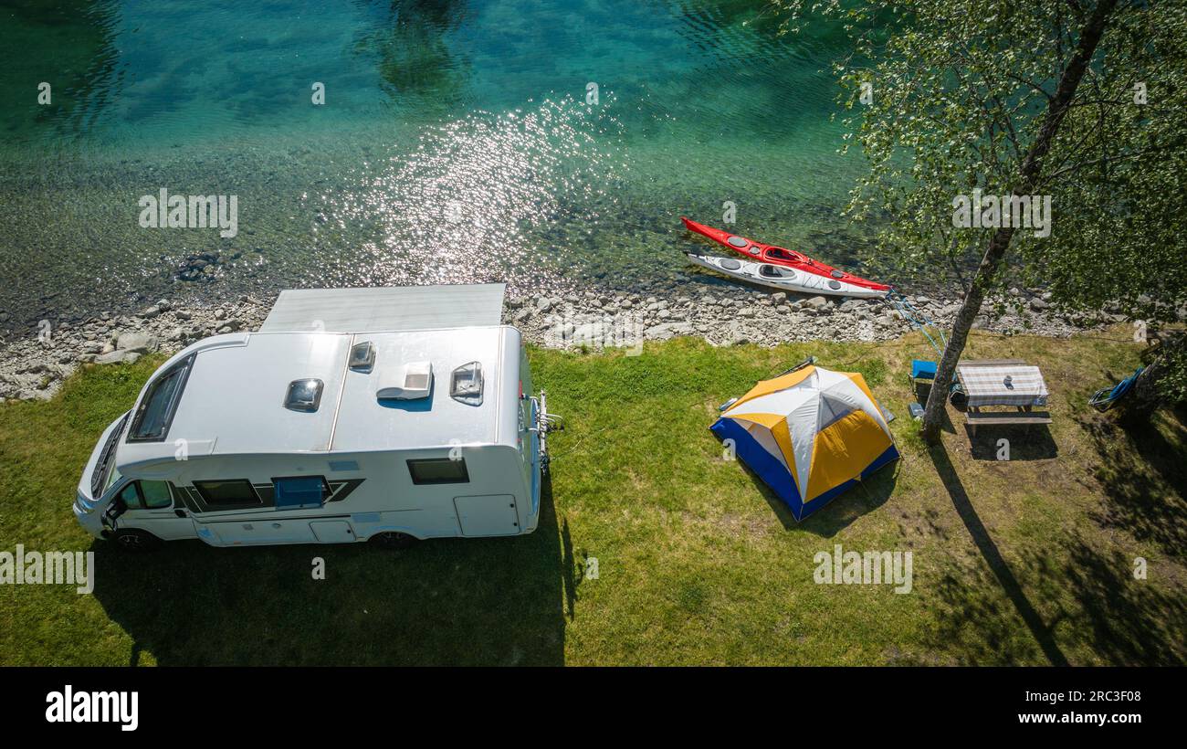 Summer Time Waterfront RV Camper Van Camping with Tent and Kayaks. Outdoors Recreation Theme. Stock Photo