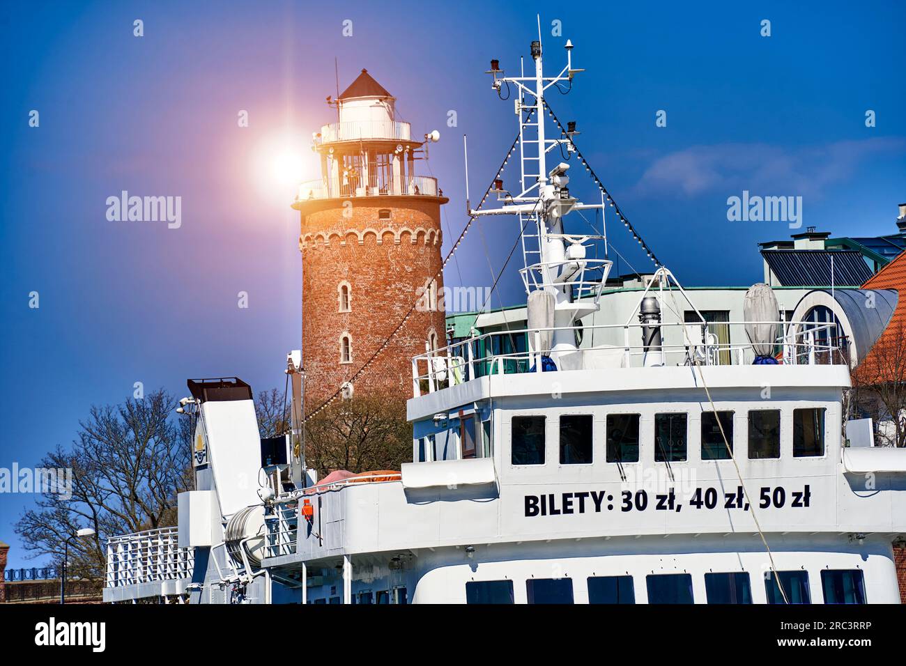 Kolberg, Poland, April 20, 2023: Excursion boat in front of the lighthouse in the backlight of the sun in the port of the Polish city of Kołobrzeg Stock Photo