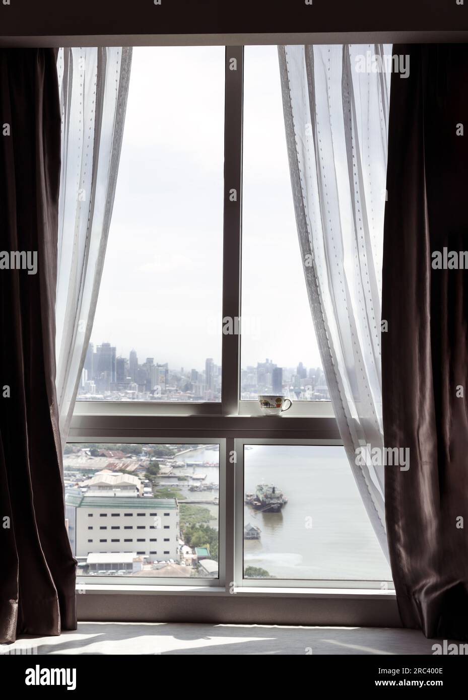A cup of morning tea or coffee with great city views by the window. Beautiful bangkok city and Chao Phraya river, Looking outside through a bedroom wi Stock Photo