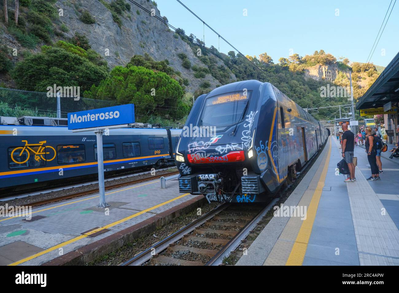 June 2023 Monterosso, Italy: regional train coming to the station in Monterosso across passengers and mountains landscape. Stock Photo