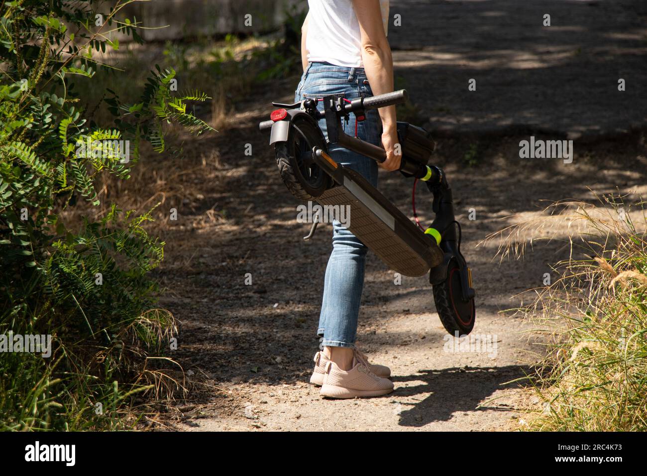 A girl holds an electric scooter in her hands in parks in Ukraine in the summer, urban electric transport Stock Photo