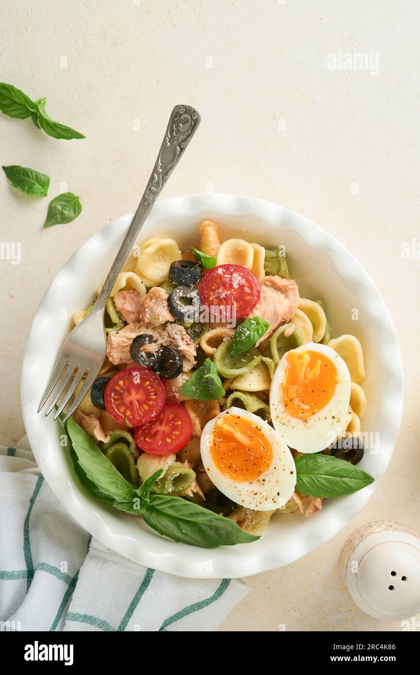 Italian pasta salad. Orecchiette pasta with tuna, tomato cherry, olive, basil and parmesan cheese in plate on grey stone or concrete background. Tradi Stock Photo