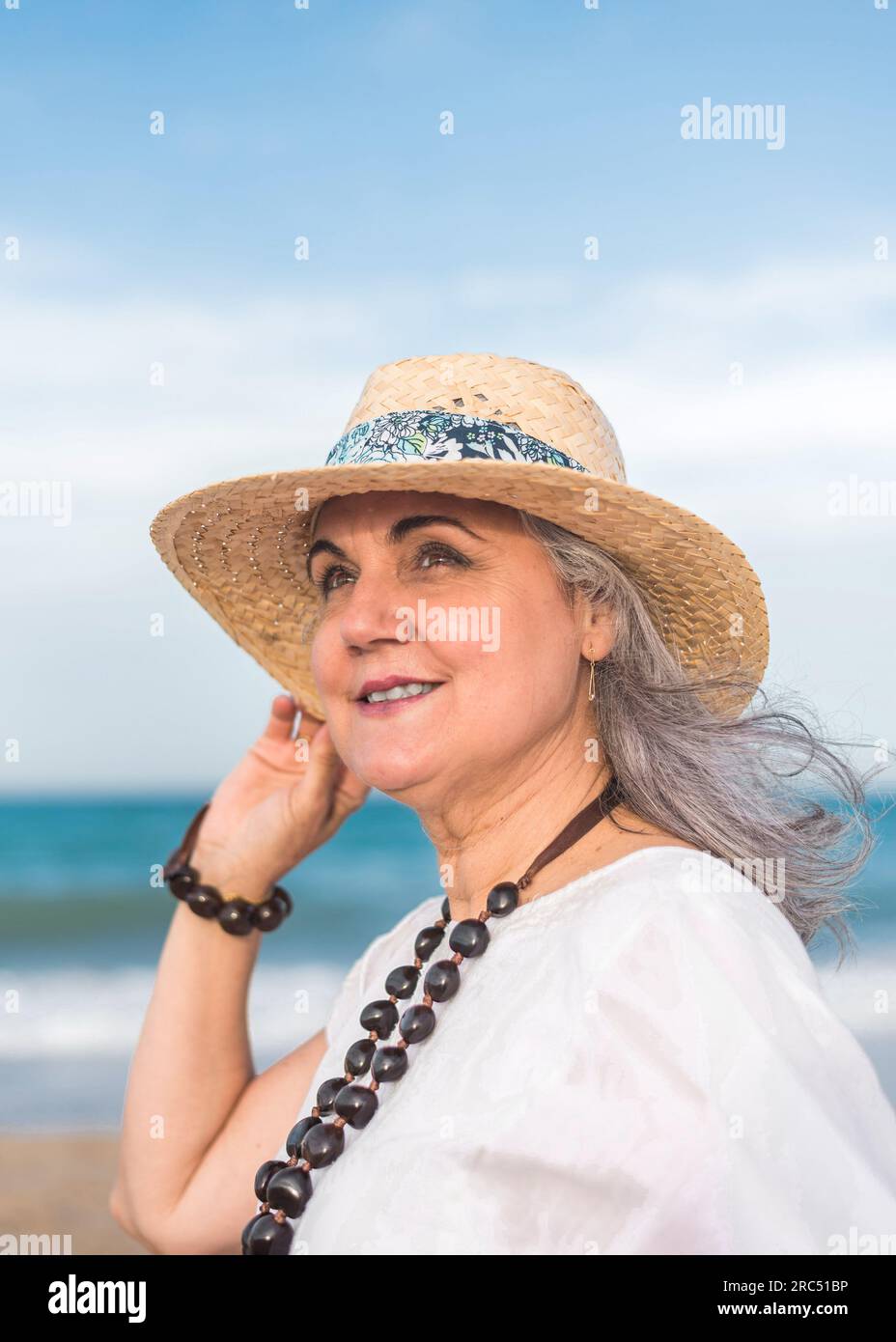 Elderly female with gray hair wearing straw hat and white dress looking