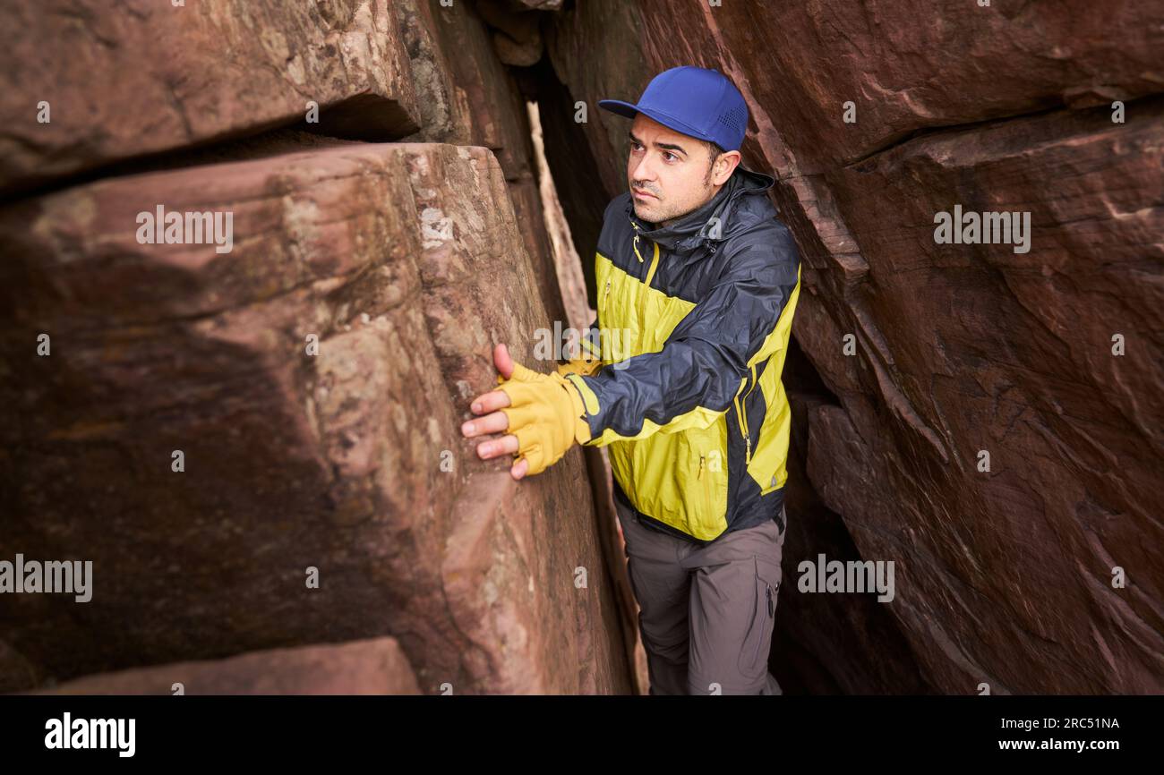 Hispanic traveler climbing through passage in cave while exploring rocky mountain during trip in Spain Stock Photo