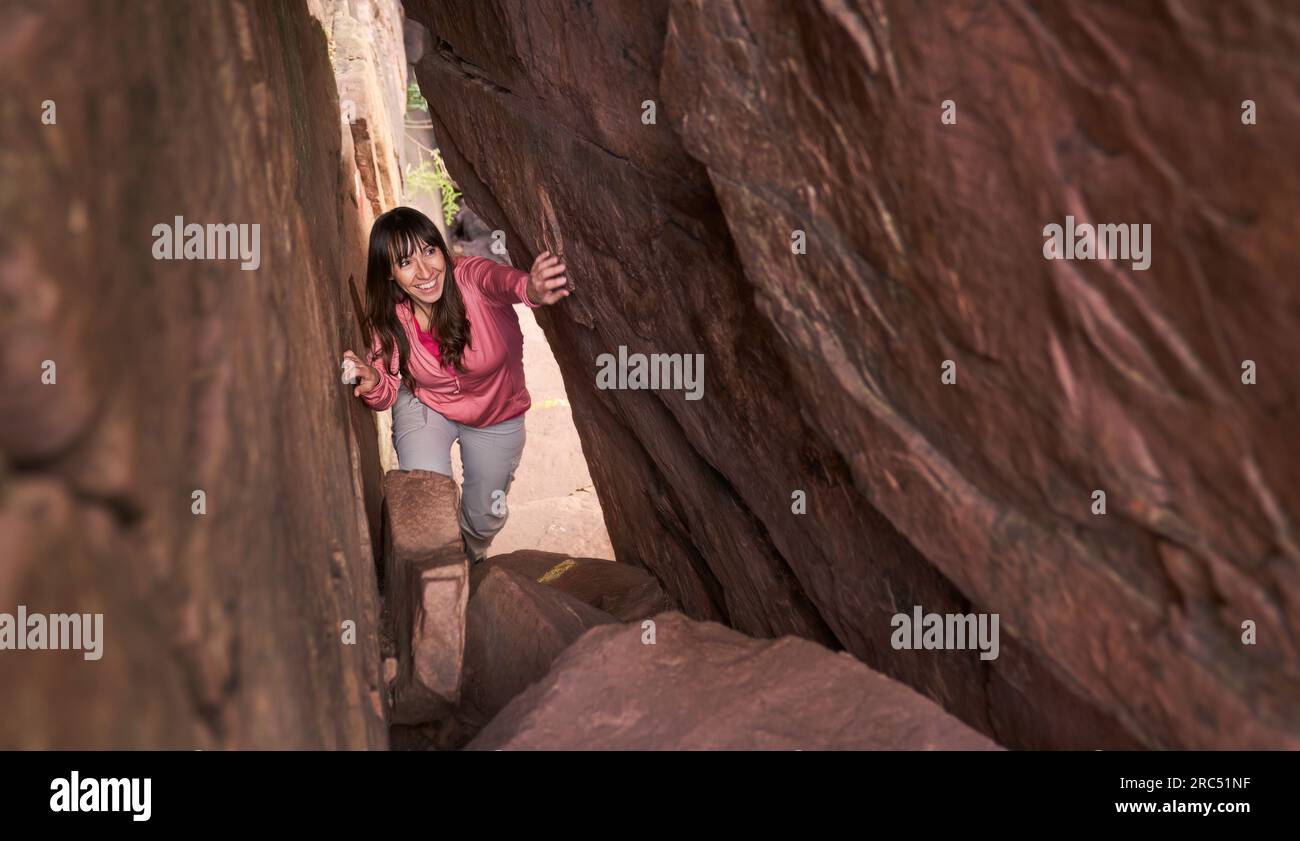 From above satisfied Hispanic lady in casual clothes touching rocky walls while exploring gap in mountain in Spain Stock Photo