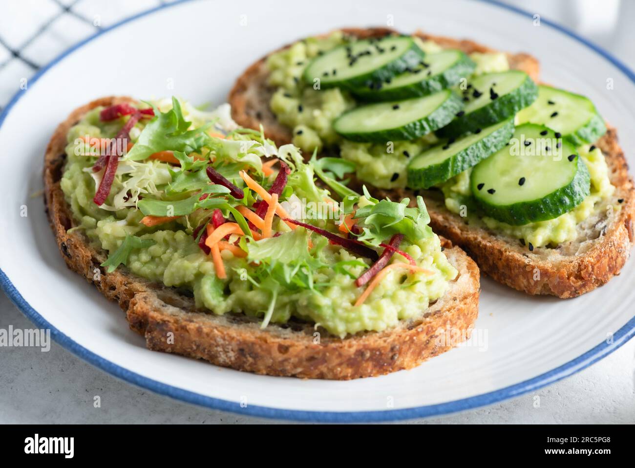 Avocado toast with different healthy vegan toppings. Cucumber, mixed greens, grated beet and carrot with seeds and olive oil. Healthy food Stock Photo