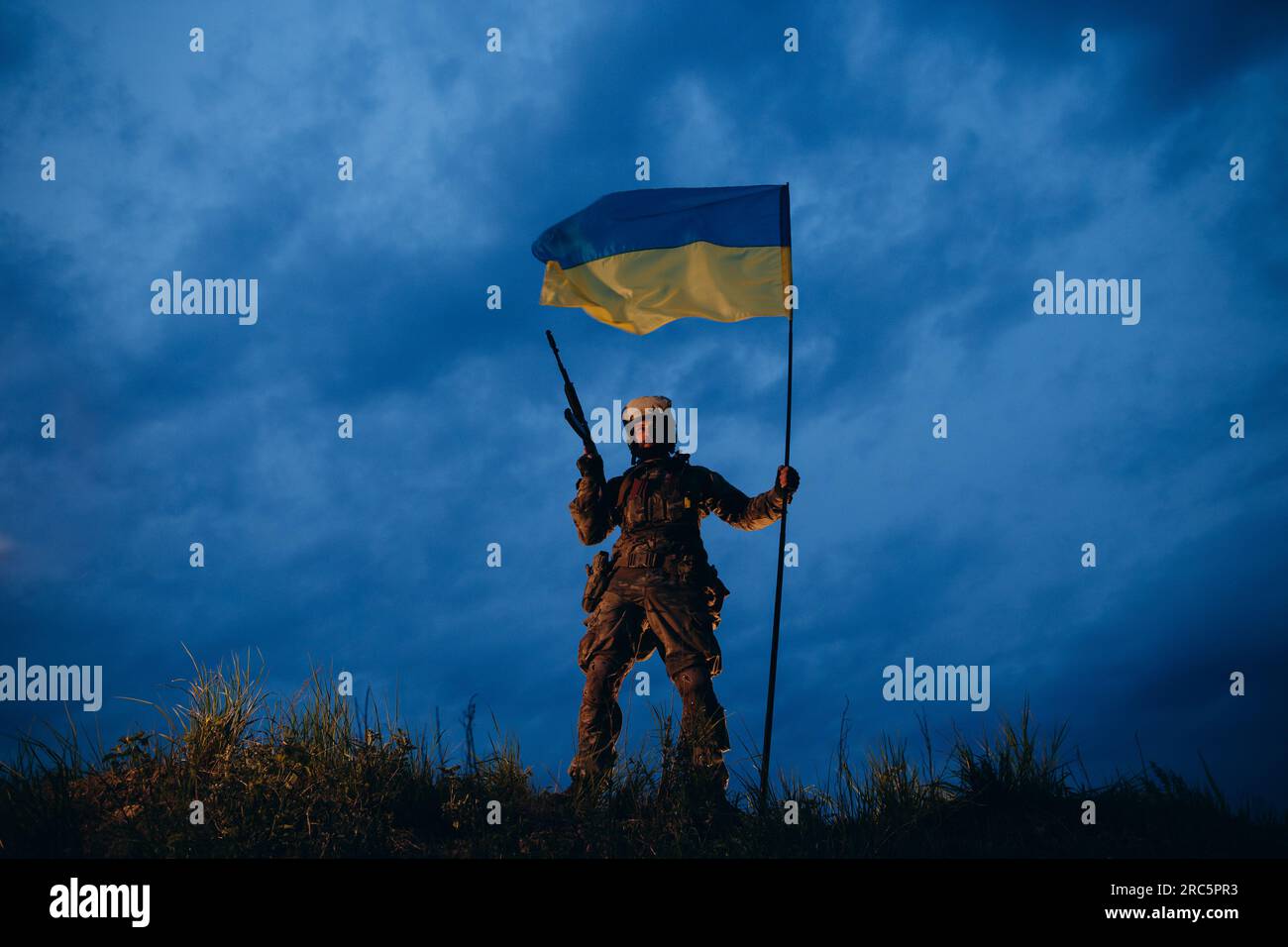 An evening portrait of Ukrainian soldier with rifle and natioal flag ...