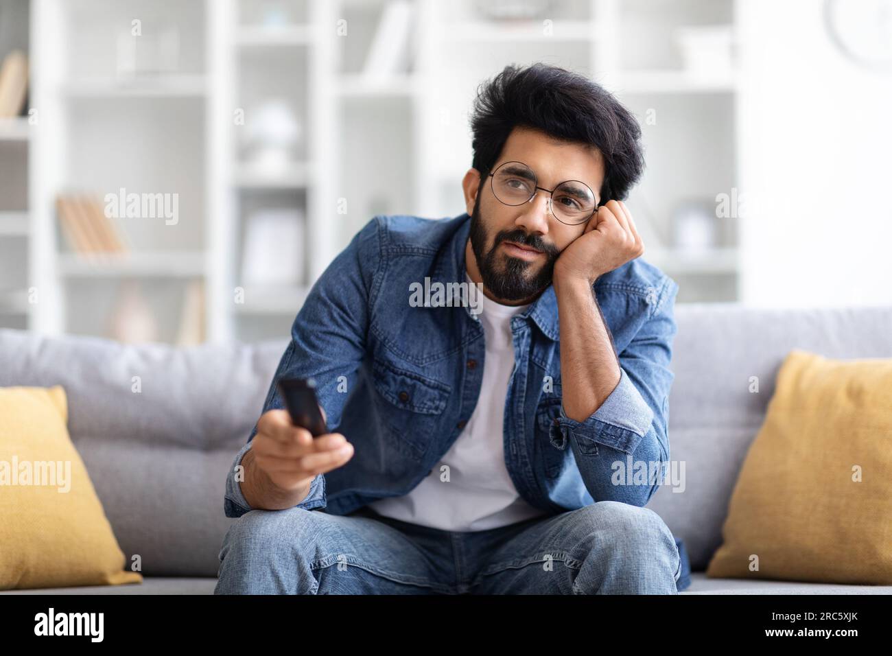 Portrait Of Bored Young Eastern Man Watching TV At Home Stock Photo
