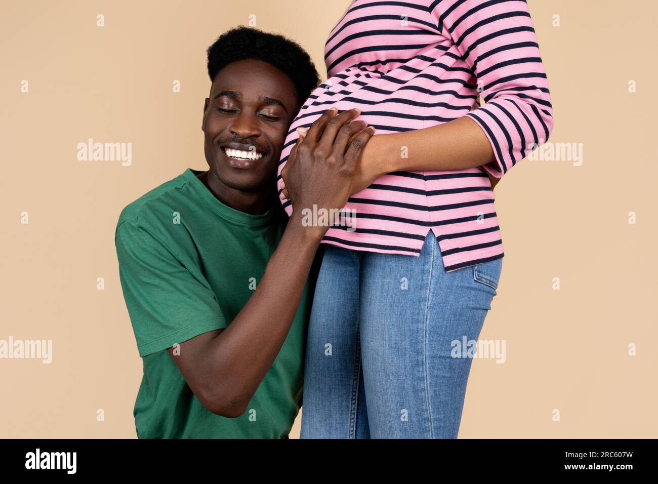 Happy millennial african american husband listens to baby in woman with ...