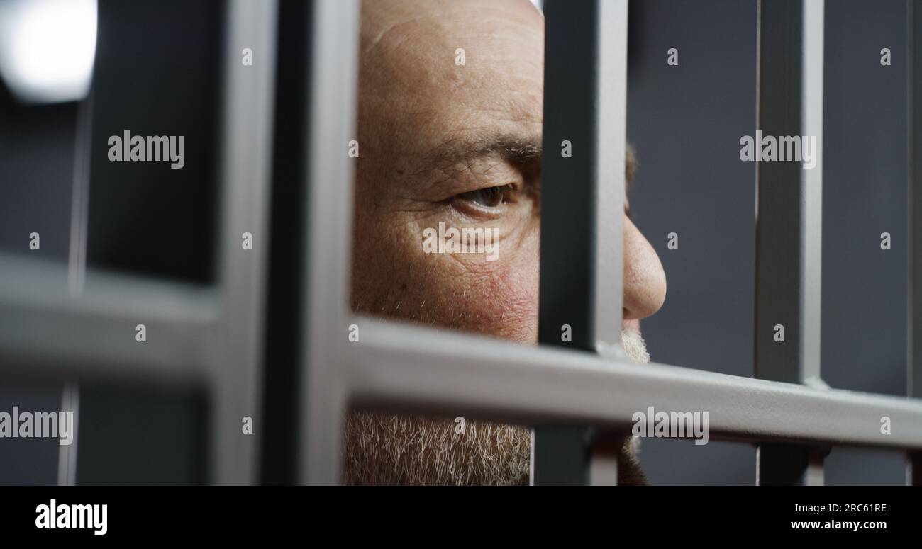 Face close up of depressed elderly prisoner standing behind metal bars