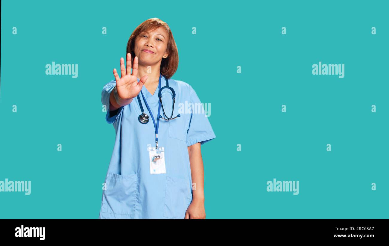 Adamant uncompromising healthcare expert throwing stop hand sign, unhappy with work conditions. Assertive asian nurse doing halt gesturing, isolated over blue studio background Stock Photo