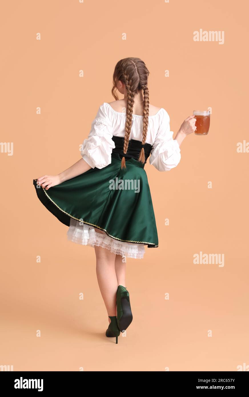 Beautiful Octoberfest waitress with beer dancing on beige background ...