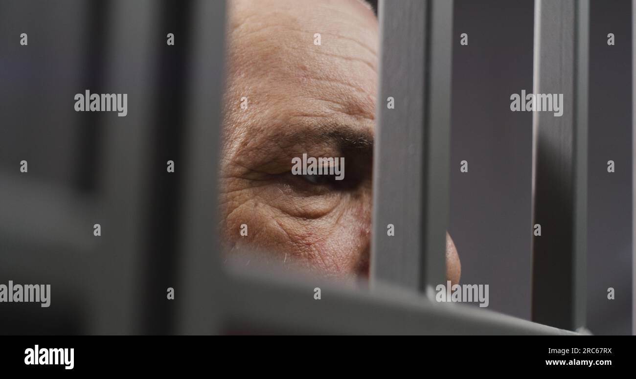 Face close up of depressed elderly prisoner standing behind metal bars