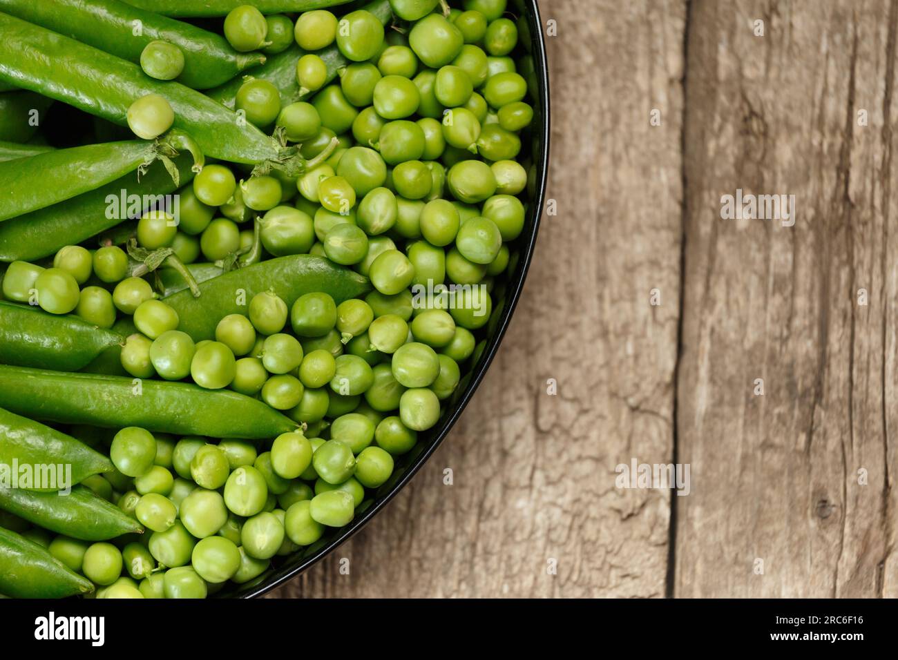 Green pea pods and shelled organic fresh peas in a round black plate on an aged wooden background, top view, copy space. Vegetable protein, healthy pr Stock Photo