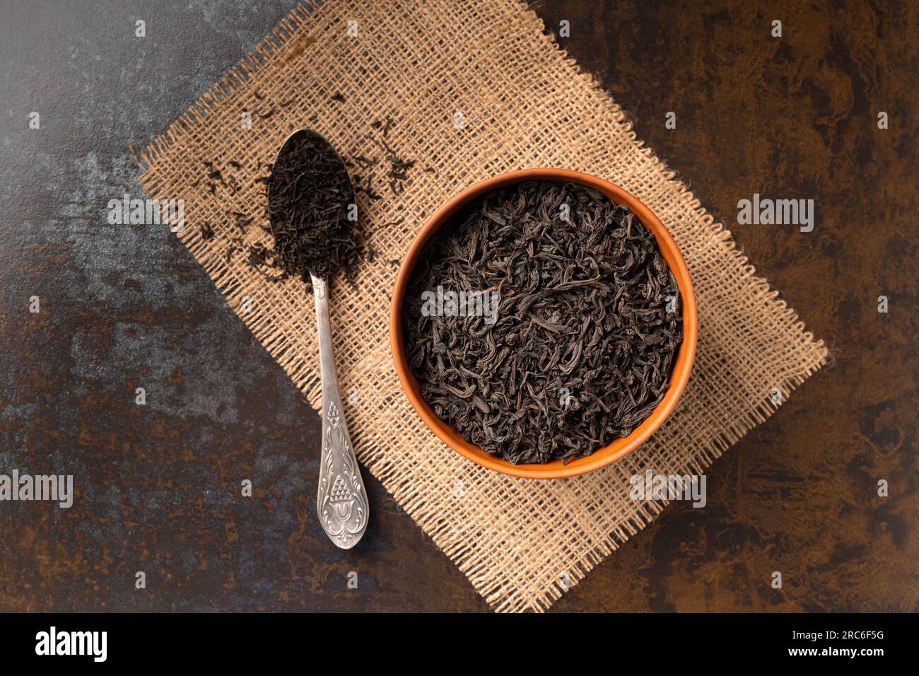 Dry black tea leaves in a clay bowl and a vintage spoon on a dark