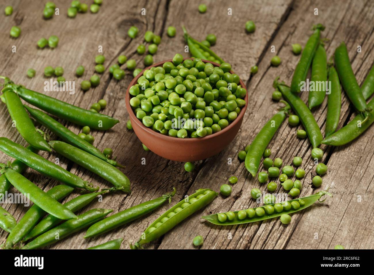 Fresh organic green peas in closed and open pods, scattered pea seeds, shelled green peas in a clay bowl on an aged wooden background Stock Photo
