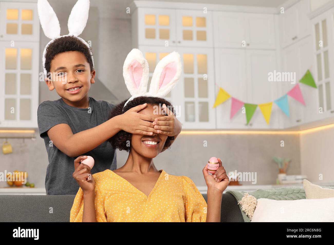 Cute African American son covering his mother's eyes with hands while ...
