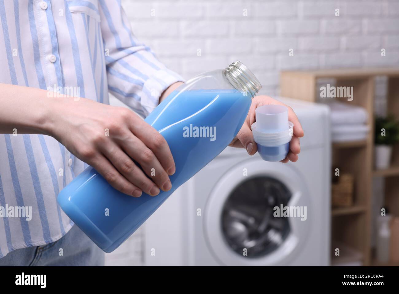 Woman pouring fabric softener from bottle into cap for washing clothes