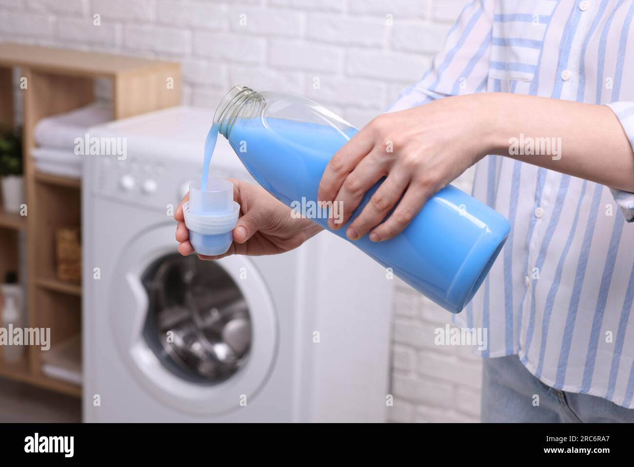 Woman pouring fabric softener from bottle into cap for washing clothes
