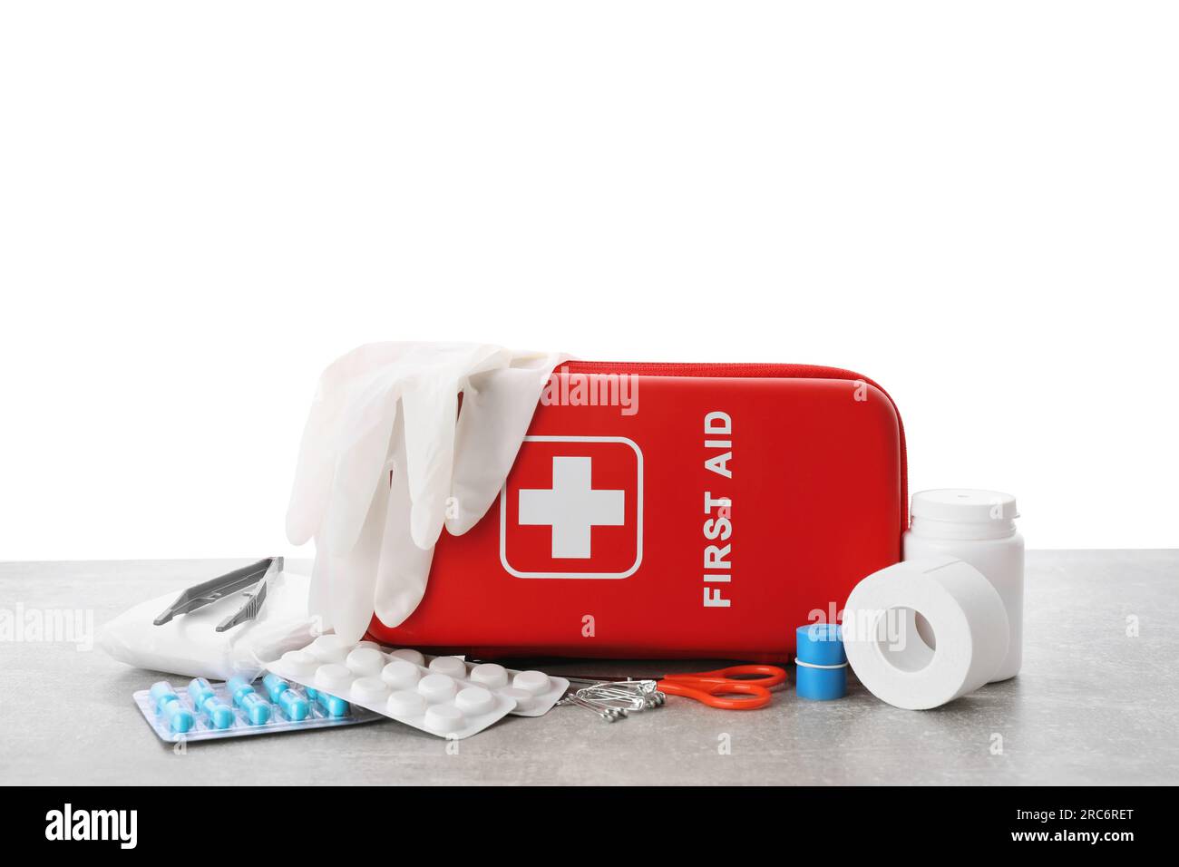 First aid kit, scissors, gloves, pills, plastic forceps and elastic bandage on light grey table