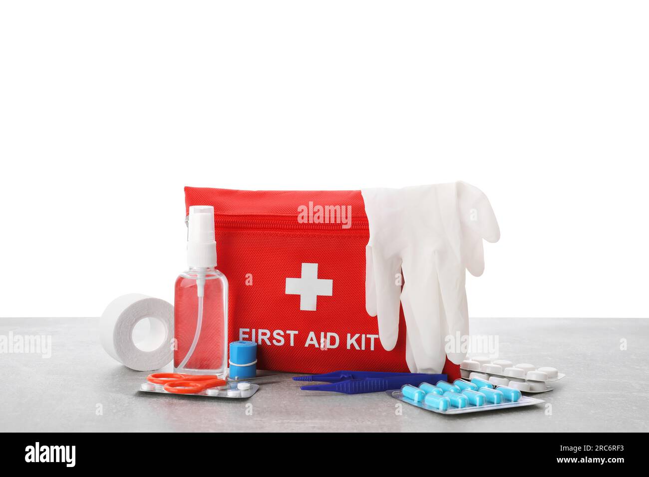 First aid kit, scissors, gloves, pills, plastic forceps and elastic bandage on light grey table