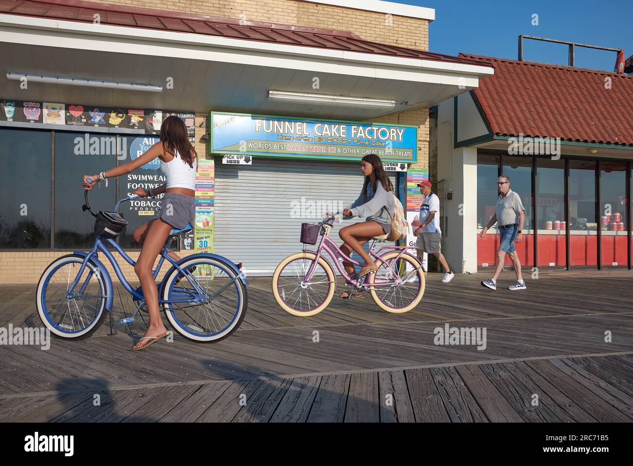 Teenage girls ride retro style bicycles on the Rehoboth Beach boardwalk on a summer morning. Stock Photo