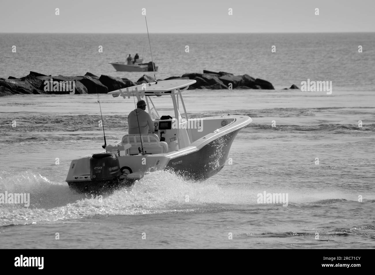 A man sails his outboard motorboat out of the channel and into open water during the summer recreational boating season. Stock Photo