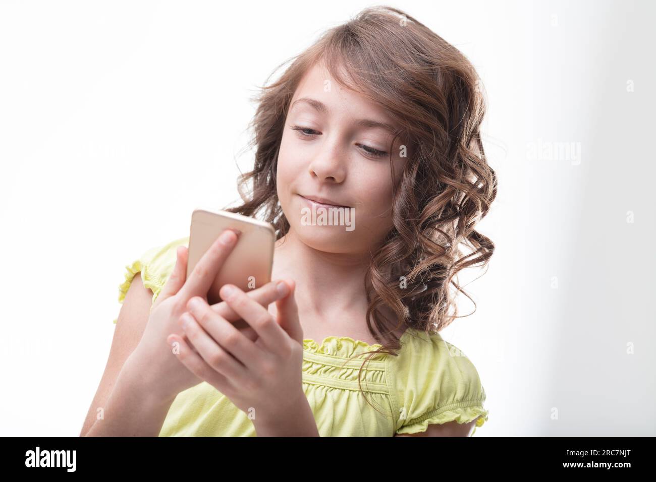Competently using a smartphone, a curly-haired girl in green epitomizes the digital generation Stock Photo