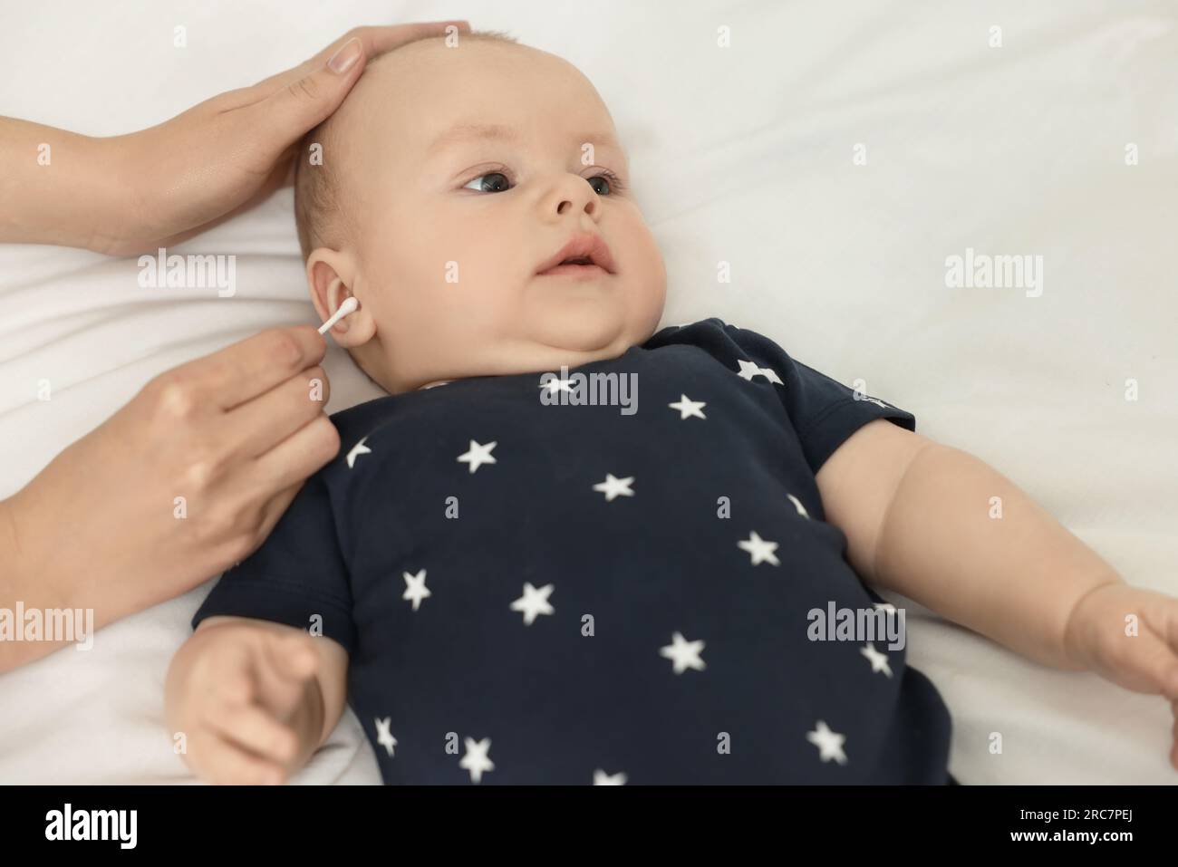 Mother cleaning ears of her baby with cotton bud on bed, closeup Stock