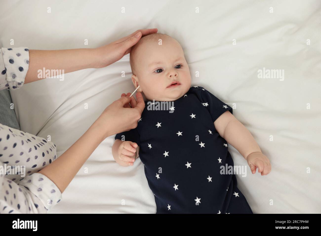 Mother cleaning ears of her baby with cotton bud on bed, top view Stock