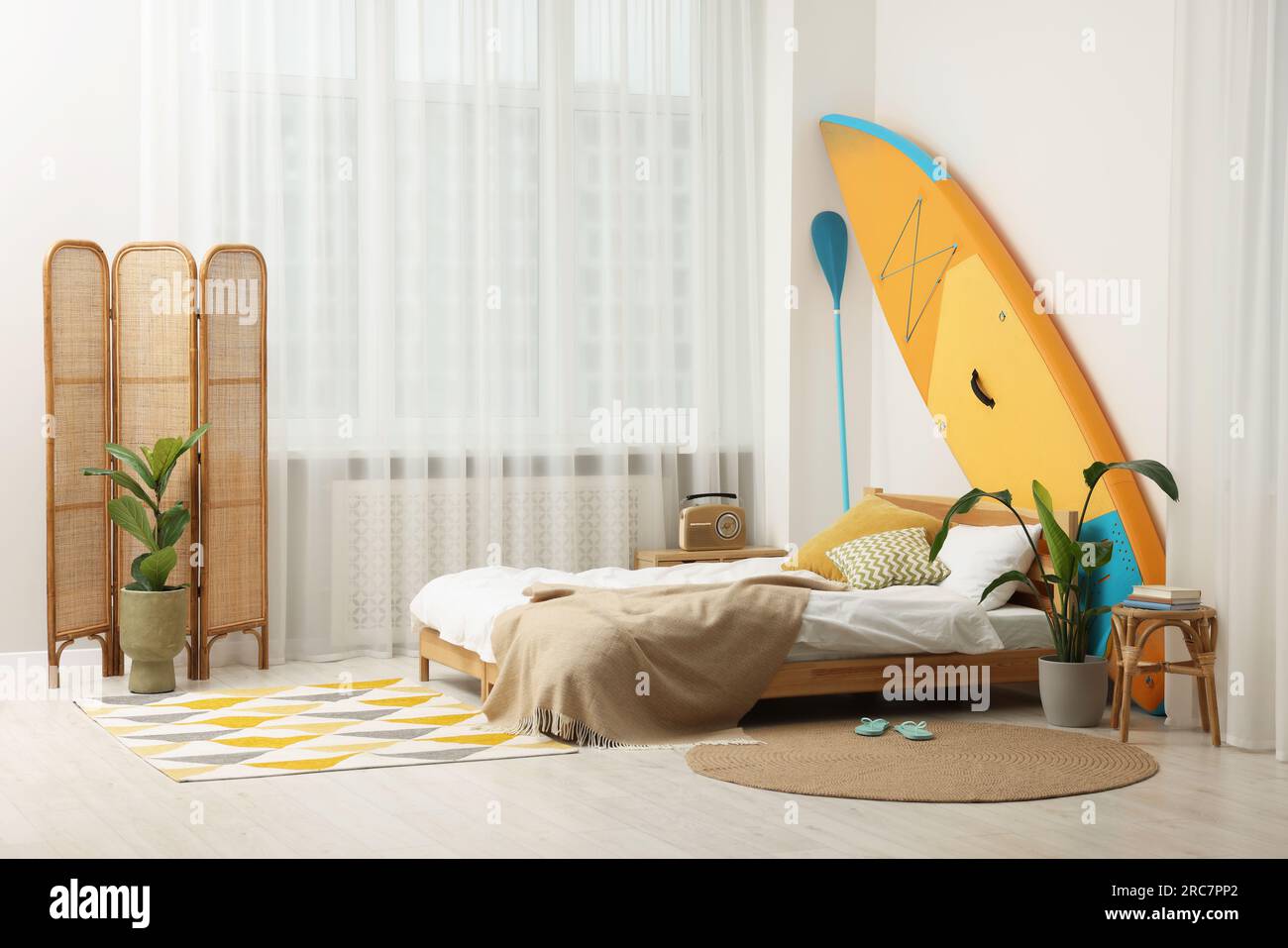 Large comfortable bed, SUP board and green houseplants in stylish ...