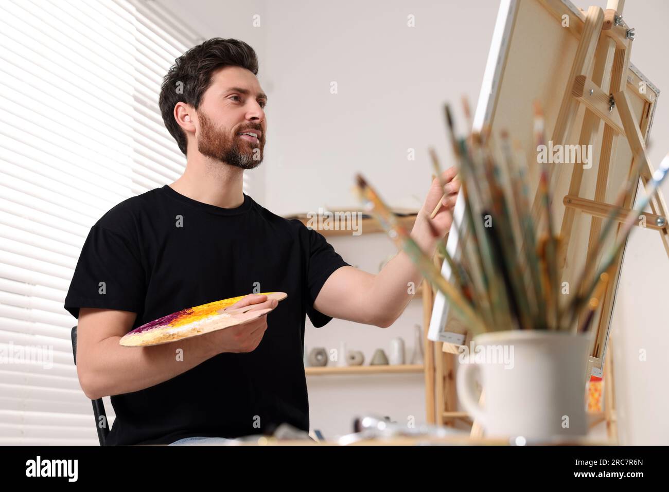 Man painting in studio. Using easel to hold canvas Stock Photo - Alamy