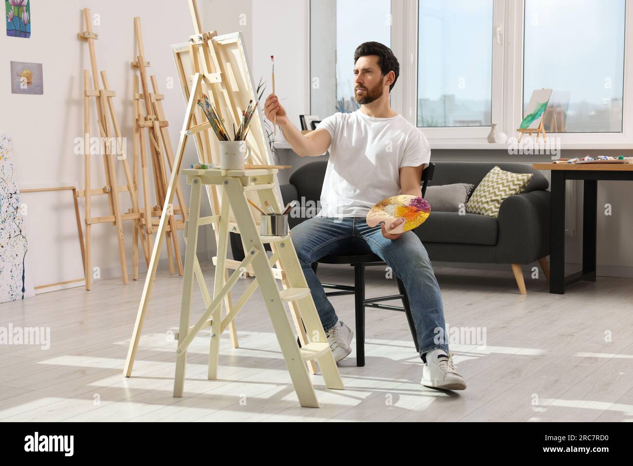 Man painting in studio. Using easel to hold canvas Stock Photo - Alamy