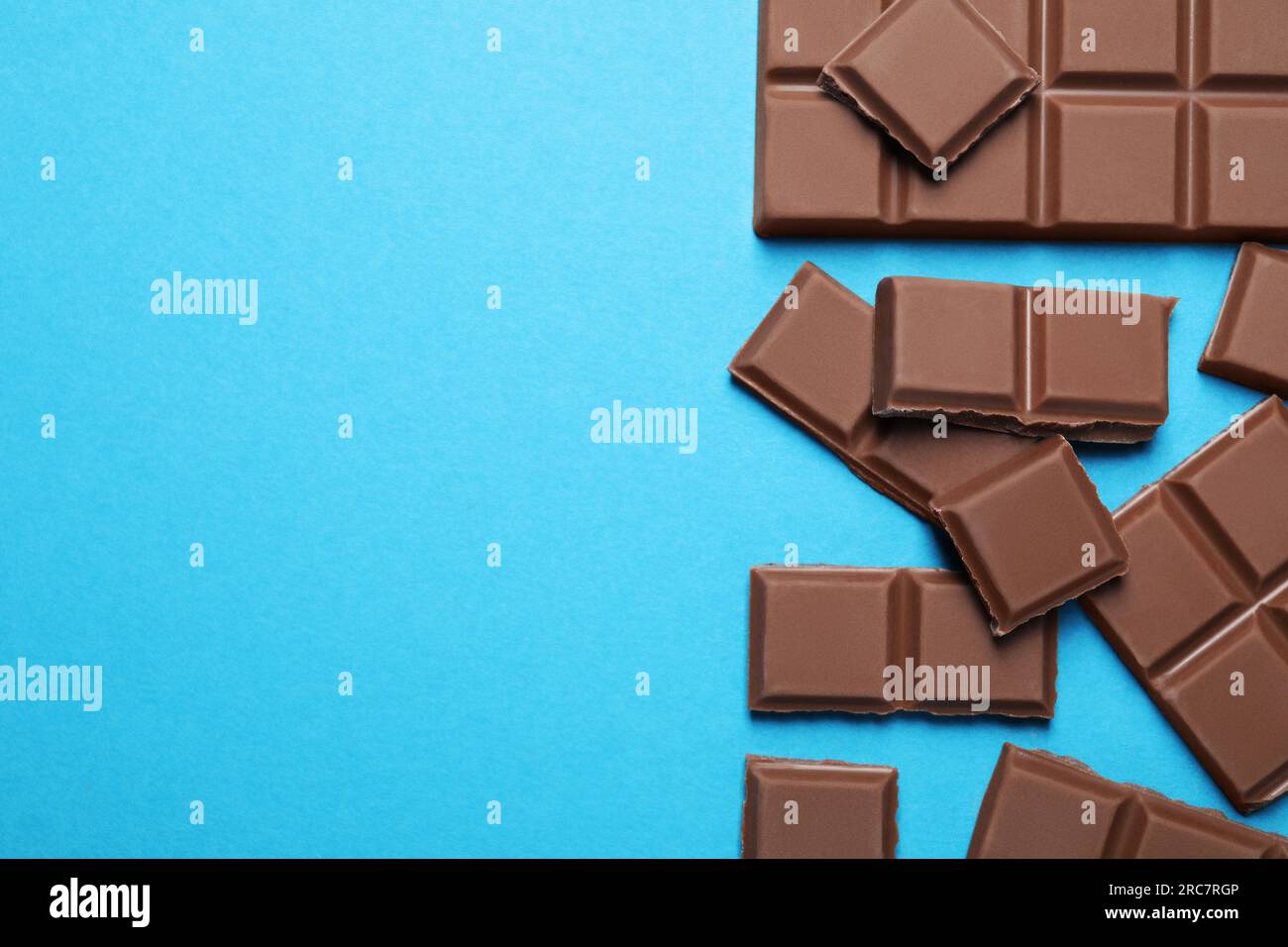 Pieces of delicious chocolate bars on light blue background, flat lay