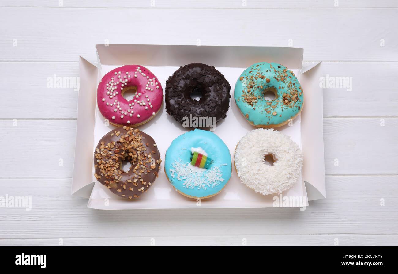Box with different tasty glazed donuts on white wooden table, top view ...