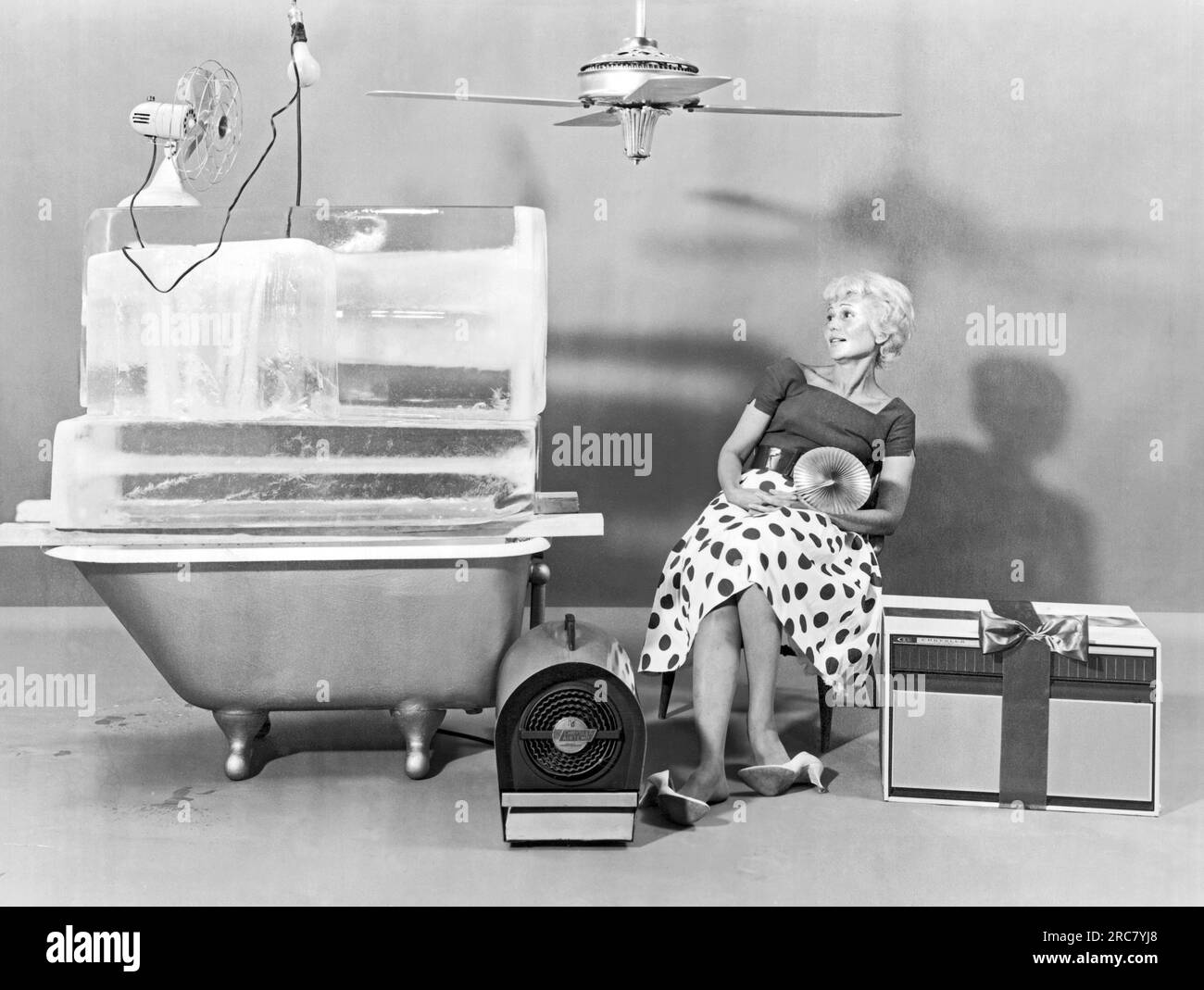 A woman trying to beat the summer heat with an assortment of cooling devices.  United States: 1961 Stock Photo