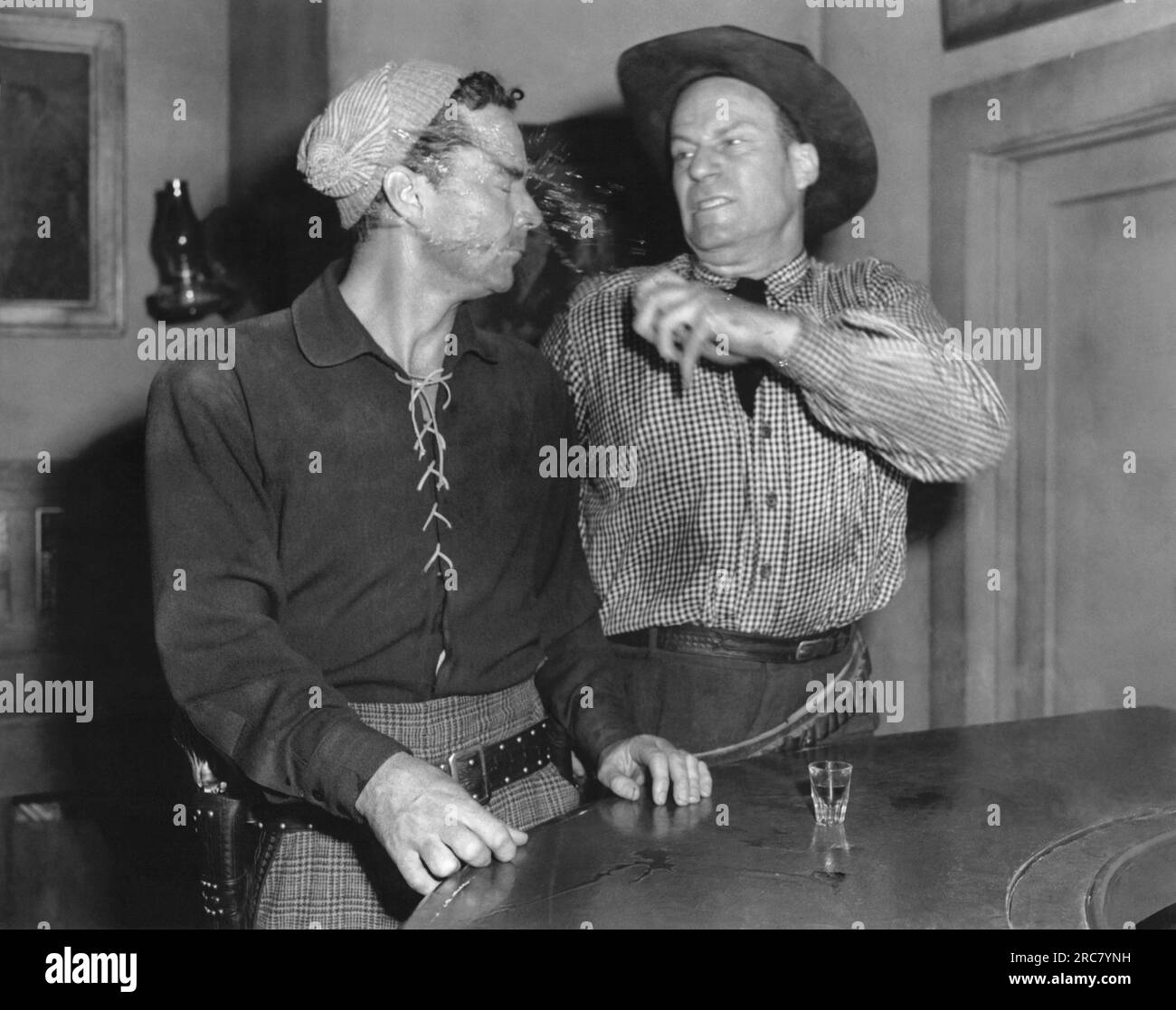 Hollywood, California:  c. 1956 An angry cowboy standing at the bar throws his drink in the face of another cowboy. Stock Photo