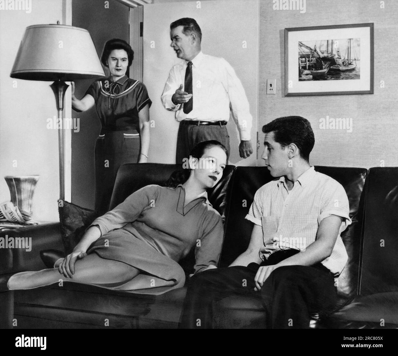 Massachusetts:  September, 1958 A teenage couple sitting on a couch gaze into each other's eyes while the parents show their disapproval. Stock Photo