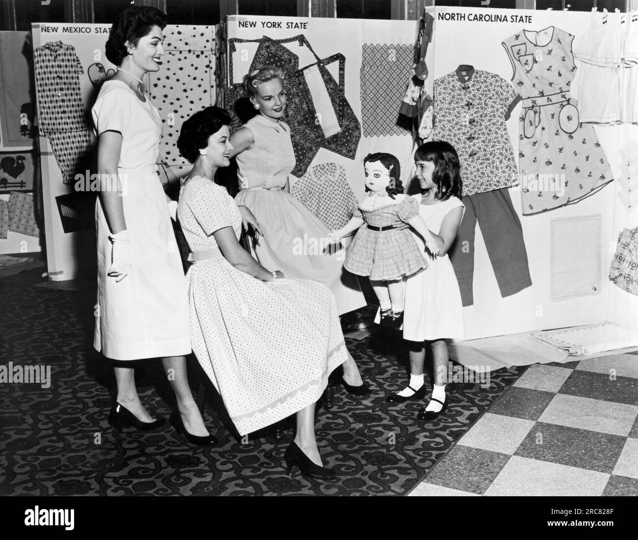 United States:  c. 1957 Dresses and other articles of clothing in this photograph were made by winners in the National Cotton Bag Sewing Contest, a competition for women who sew with the cotton sacks used in packaging products. A young girl proudly holds her Raggedy Ann doll with cotton sack clothing. Stock Photo