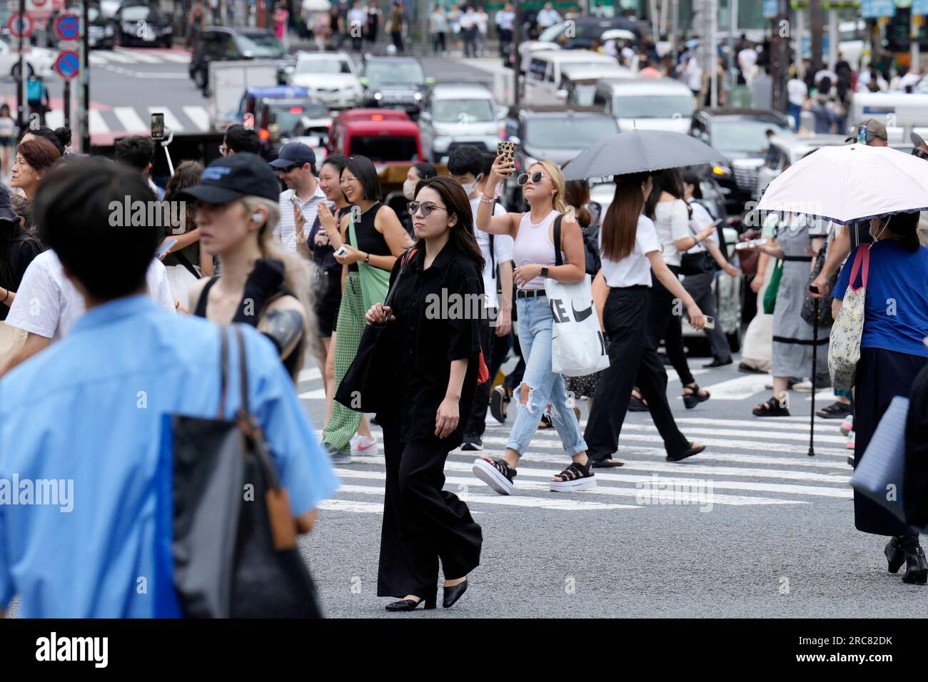 People walk cross a pedestrian crossing in Shibuya district under hot
