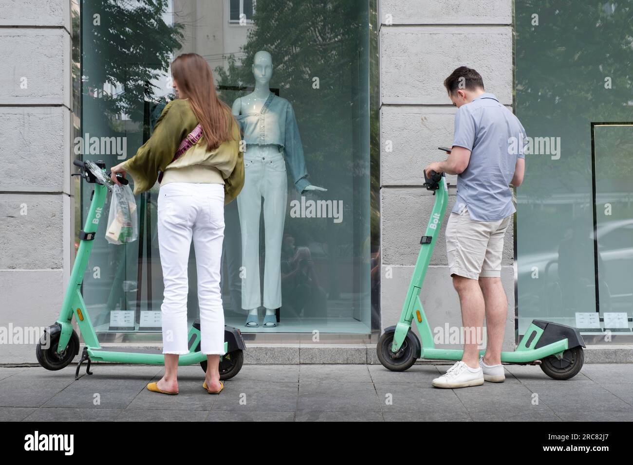 Shared electric kick scooters for rent in front of a fashion store window in Vilnius. A couple decides to rent them. E-mobility Stock Photo
