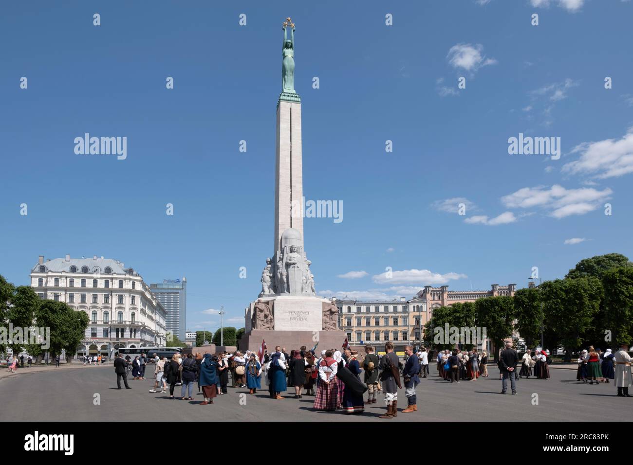 Freedom Monument in Riga, Latvia with people in traditional Latvian costumes. Memorial honors soldiers who died during the Latvian War of Independence Stock Photo