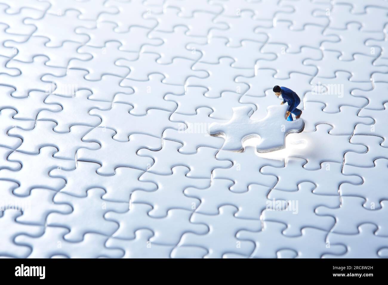 Miniature dolls fitting a white puzzle and a piece of white puzzle on the front page Stock Photo