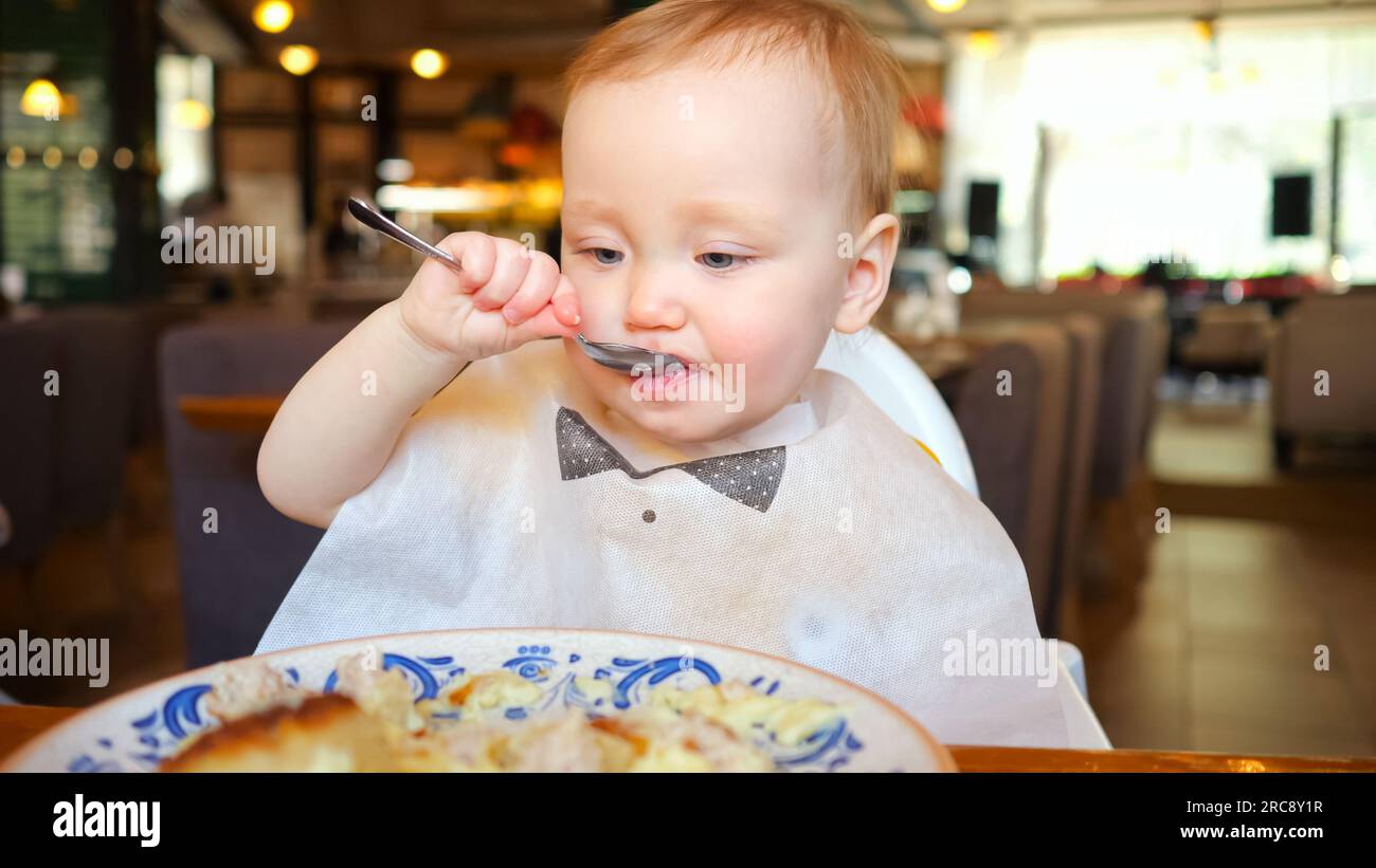 Toddler girl likes to eat food by licking fork in restaurant Stock Photo
